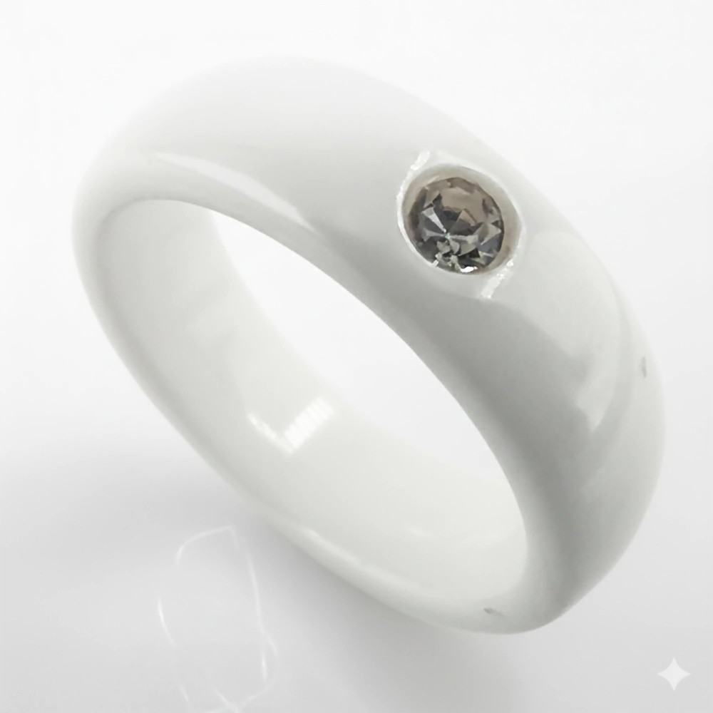 Biała ceramiczna obrączka o szerokości 6mm z pojedynczą, błyszczącą cyrkonią na jasnym tle.