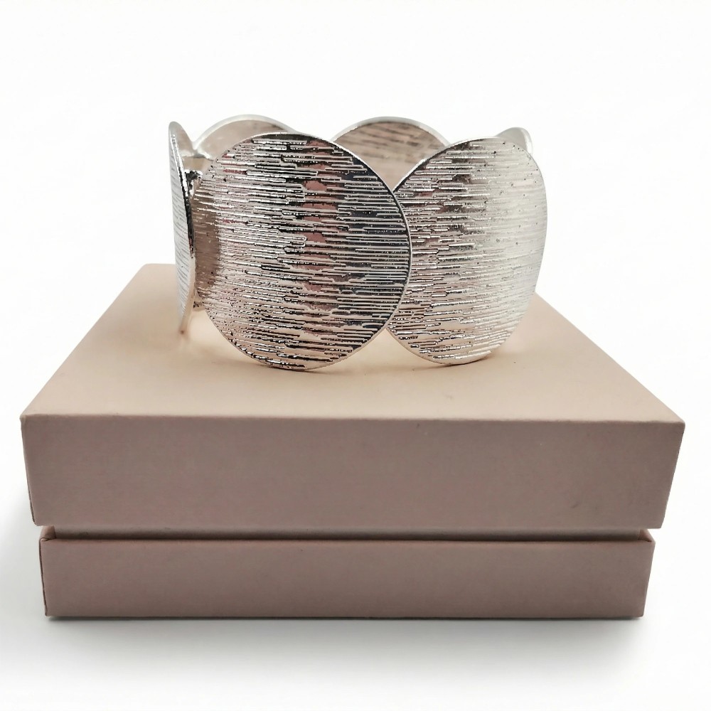 Teksturowana srebrna bransoletka bangle ułożona na eleganckim beżowym pudełku prezentowym.)